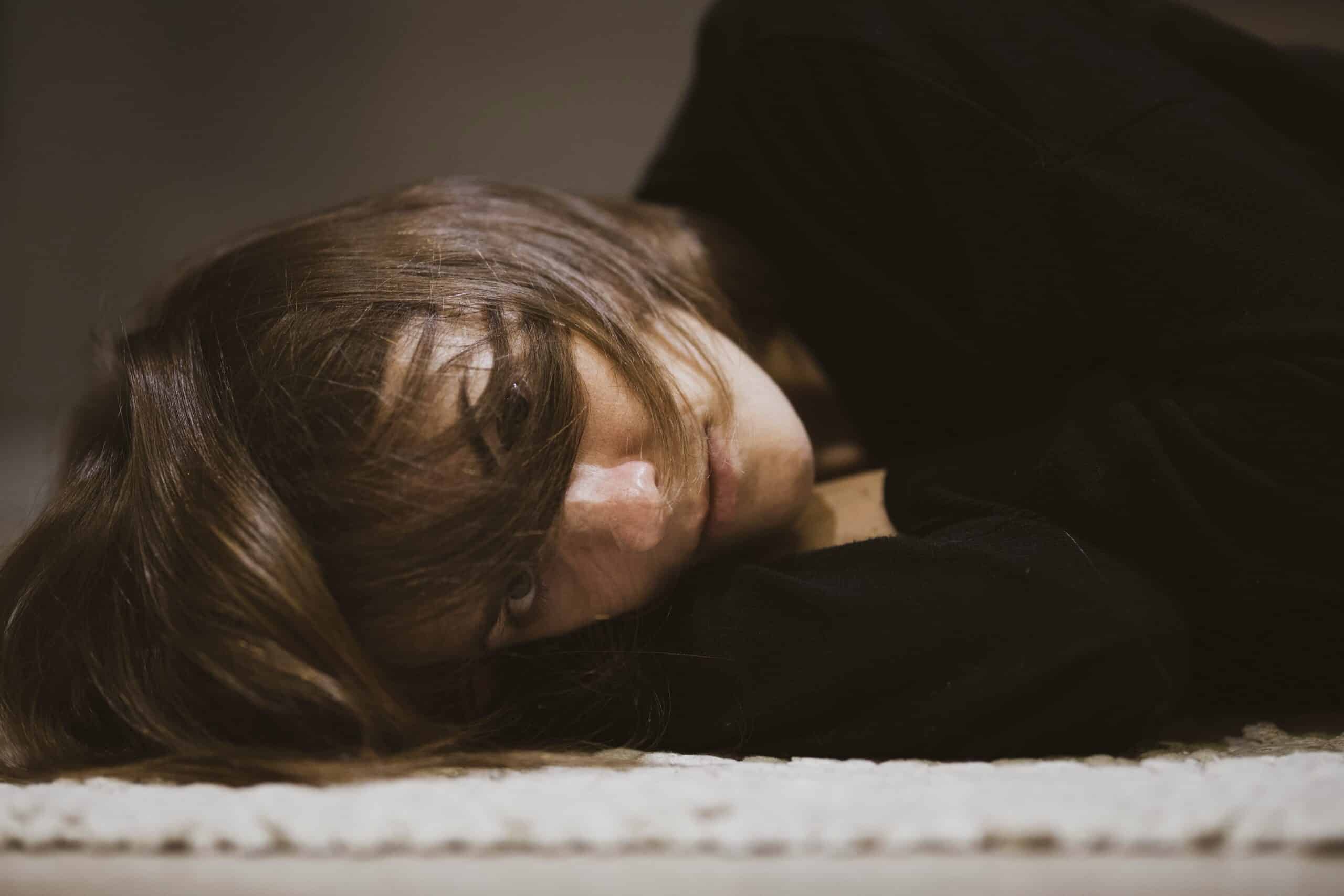 woman in long-sleeve black t-shirt and short brown hair over her face laying on the ground